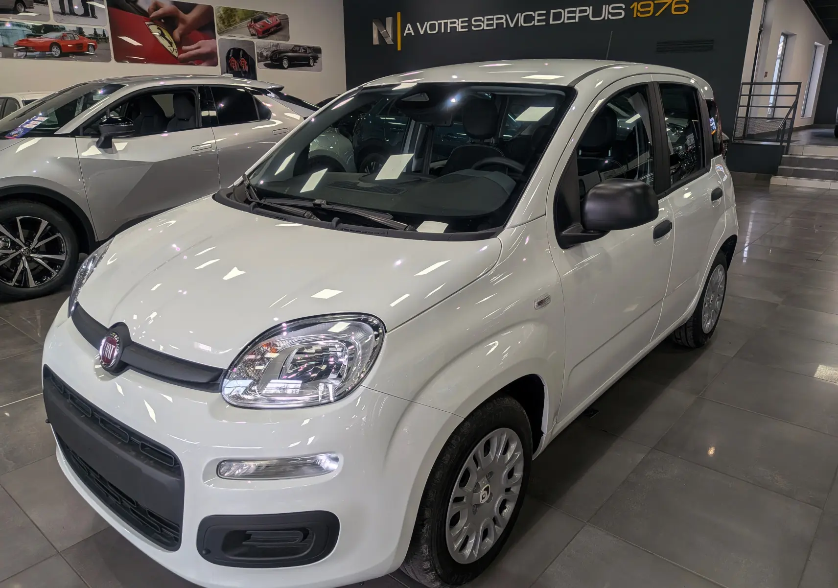 Vue 3/4 avant droite d'une FIAT Panda 1.0 70 CH Hybrid City blanche Gelato en showroom avec détails noirs contrastants.