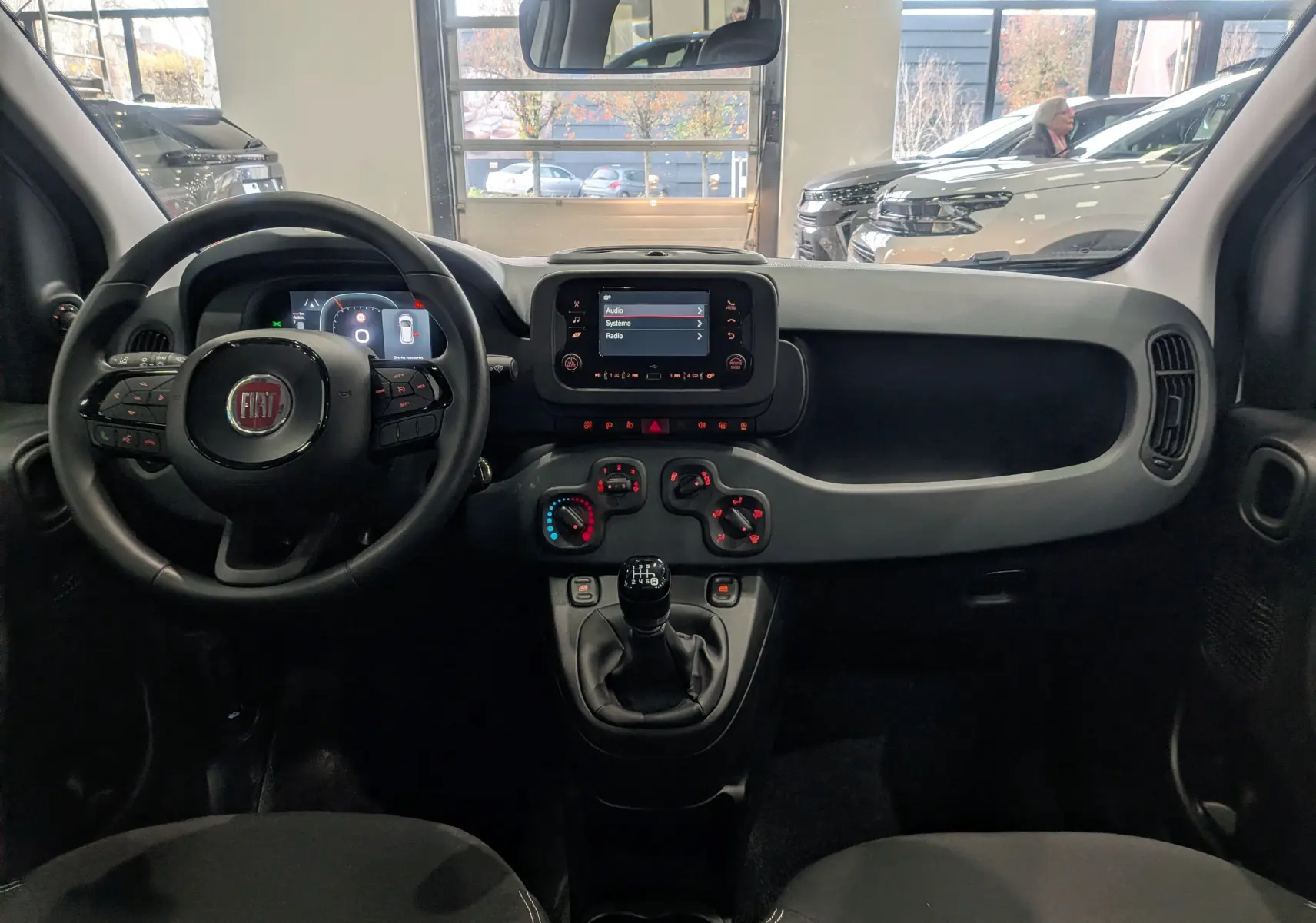Vue frontale de l'intérieur de la Fiat Panda 1.0 Hybrid 2025 blanc Gelato avec tableau de bord noir et console centrale manuelle.