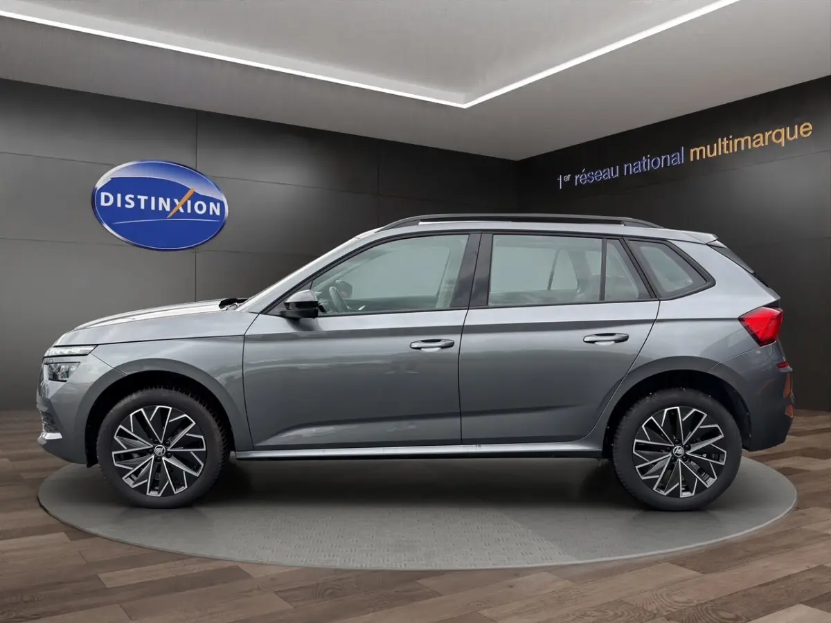 SKODA KAMIQ gris foncé en profil côté gauche, avec jantes bi-ton et toit noir visible en showroom.