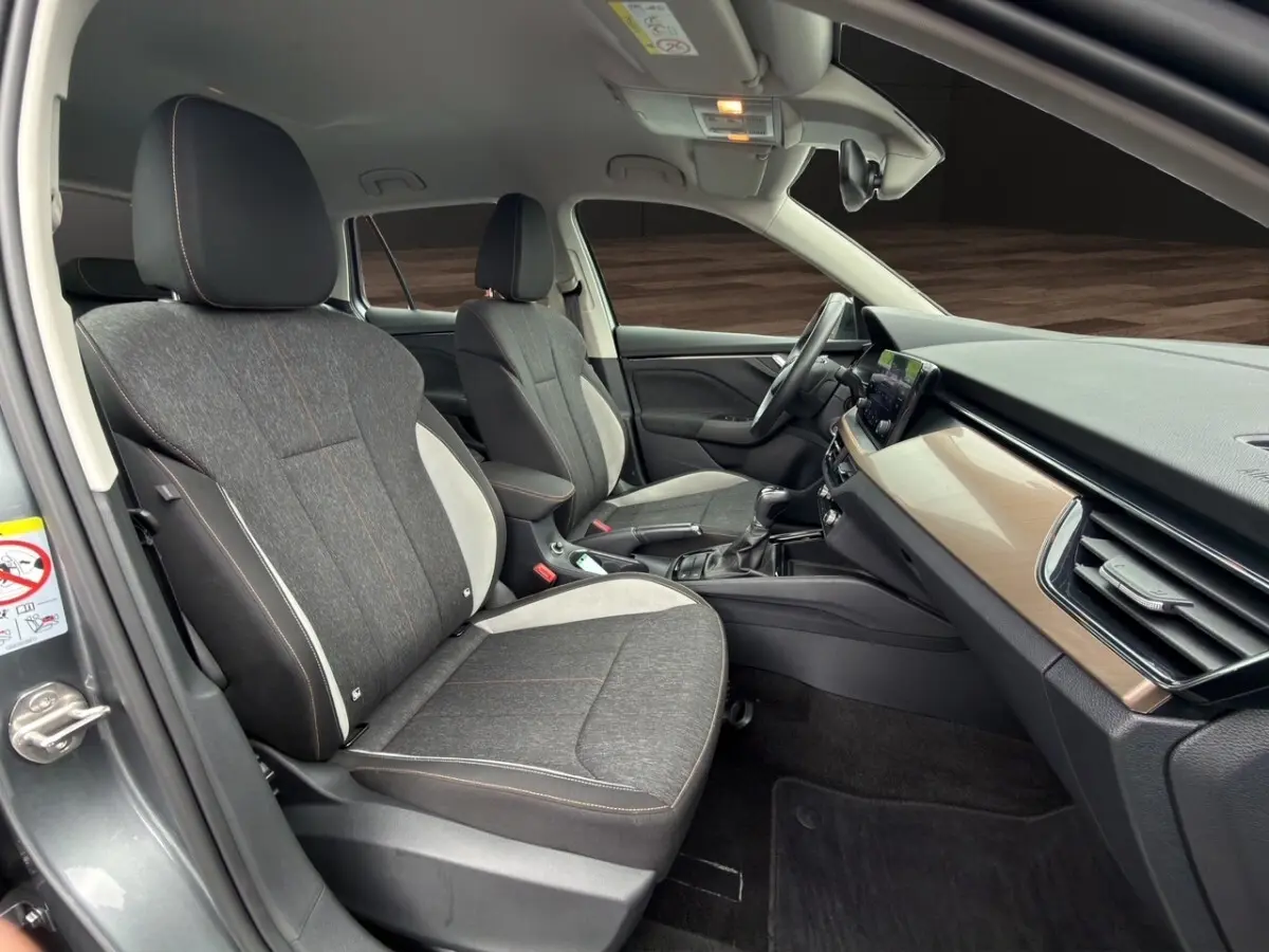 Vue intérieure côté gauche du Skoda Kamiq 2023 gris foncé, sièges tissu bicolore et tableau de bord bois clair.