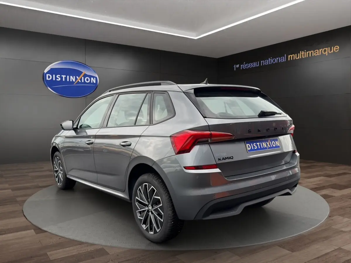 Vue 3/4 arrière droite d'un Skoda Kamiq gris foncé avec jantes bi-ton et caméra de recul en showroom.