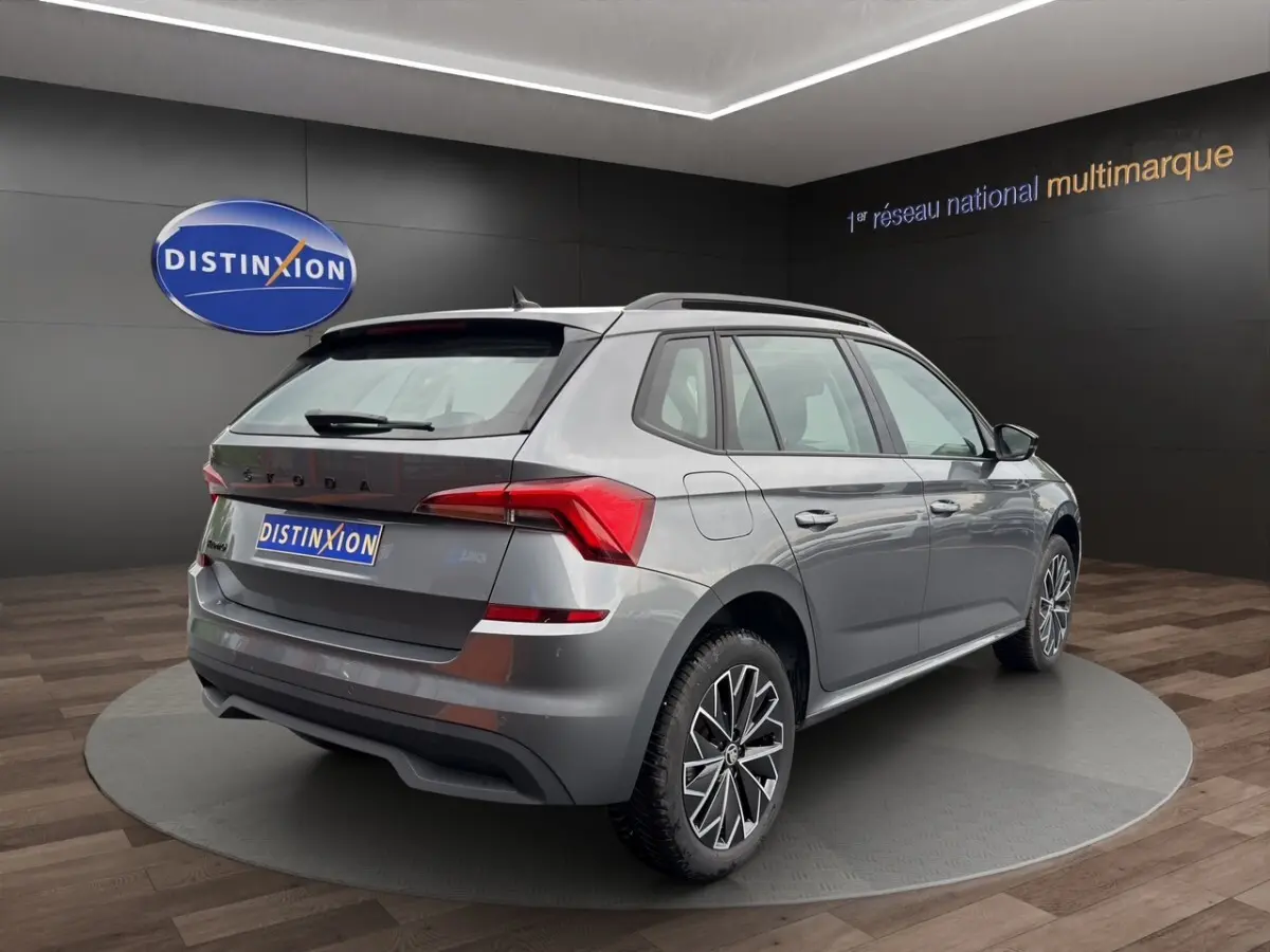 Vue 3/4 arrière droite d'un Skoda Kamiq gris foncé avec jantes bi-ton et caméra de recul en showroom.