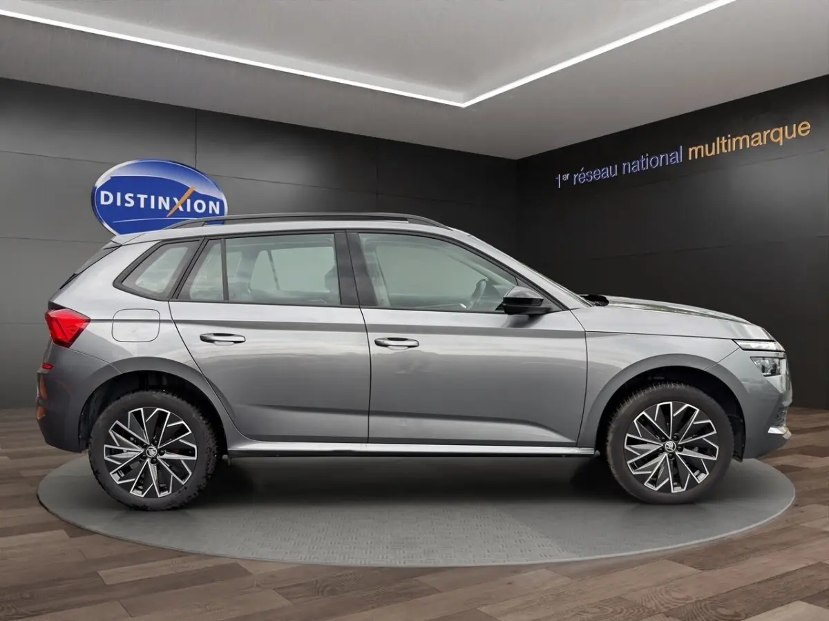 Vue de profil côté gauche d'un Skoda Kamiq gris foncé 2023 avec jantes bi-ton et barres de toit noires.