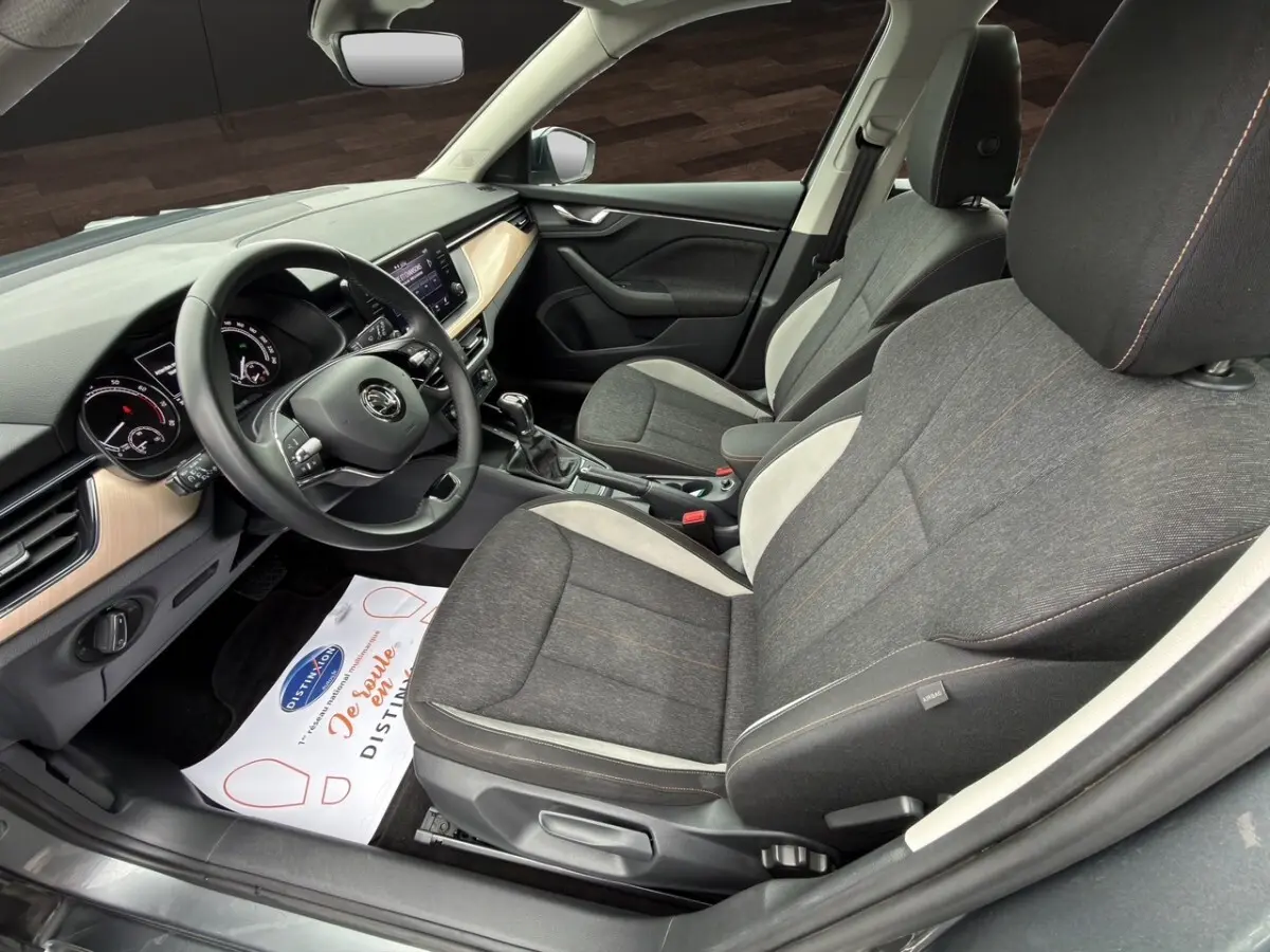 Vue intérieure côté conducteur du Skoda Kamiq 2023 gris foncé, avec sièges tissu bicolore et tableau de bord clair.