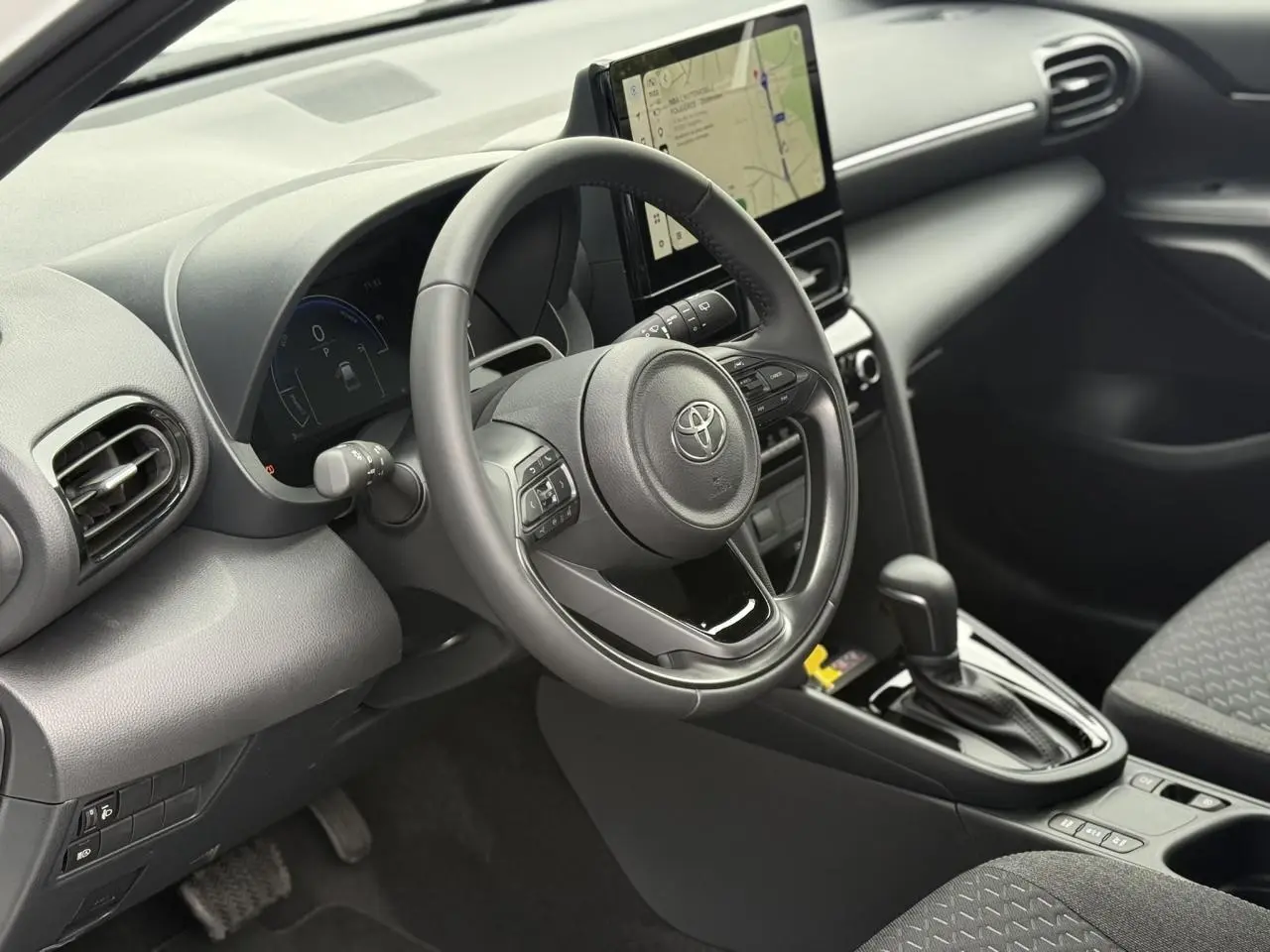 Vue intérieure côté conducteur de la Toyota Yaris Cross 2026, tableau de bord noir avec écran tactile et volant multifonction.