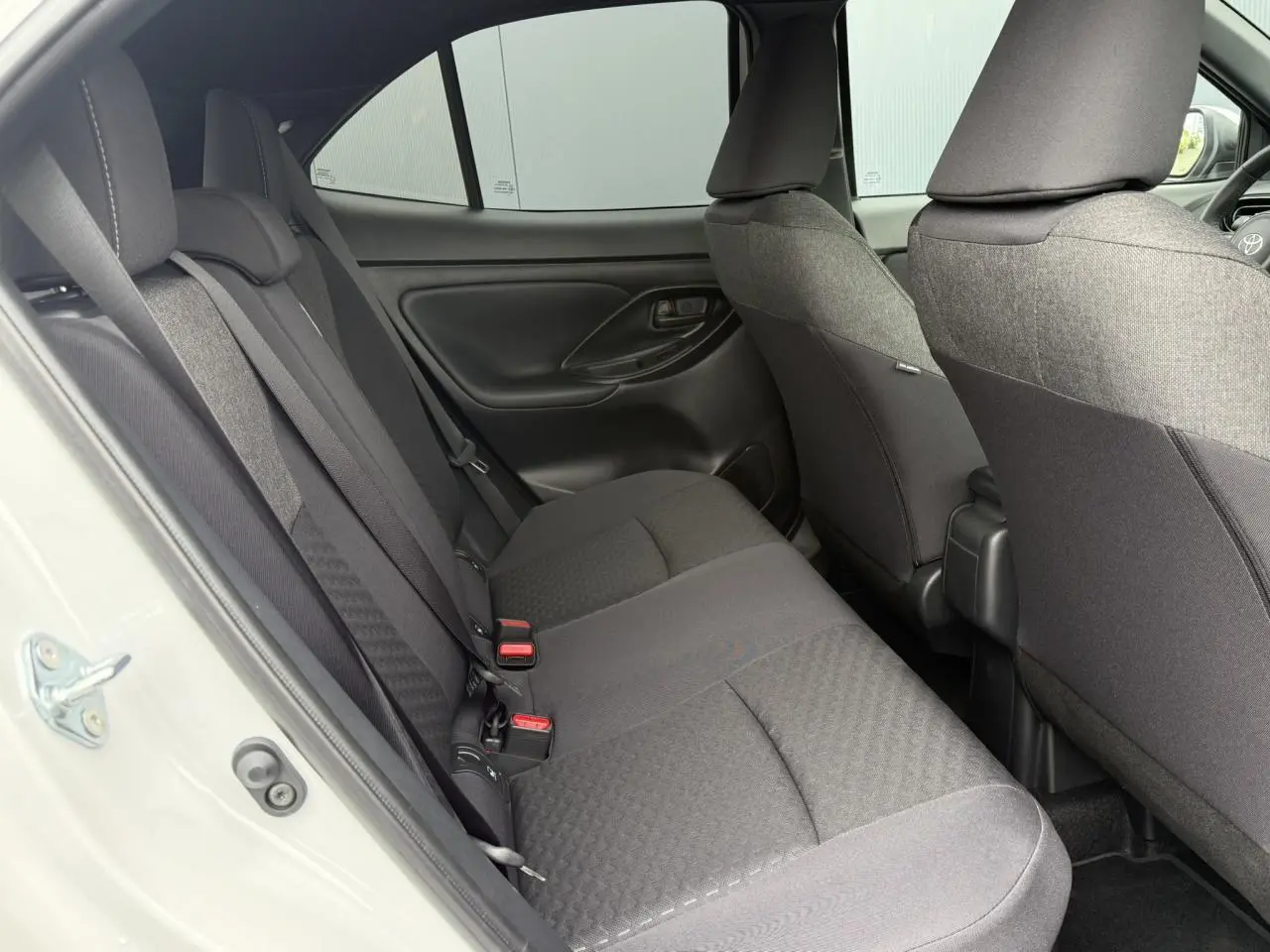 Vue intérieure côté gauche des sièges arrière noirs du Toyota Yaris Cross blanc Lunaire 2026, avec portières fermées.
