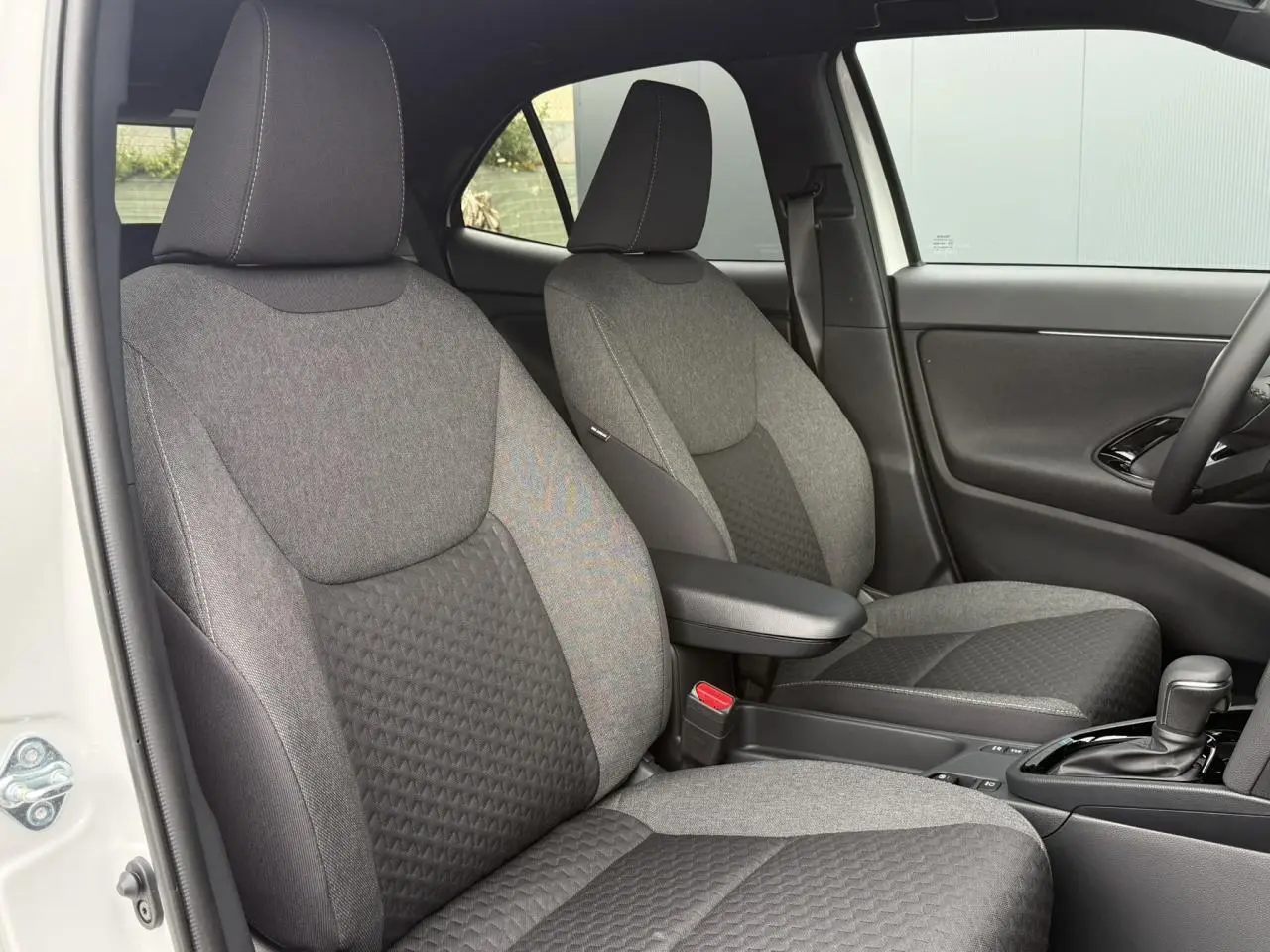 Vue intérieure côté gauche des sièges avant gris foncé et clair de la Toyota Yaris Cross 1.5 Hybrid 116 Design blanche.