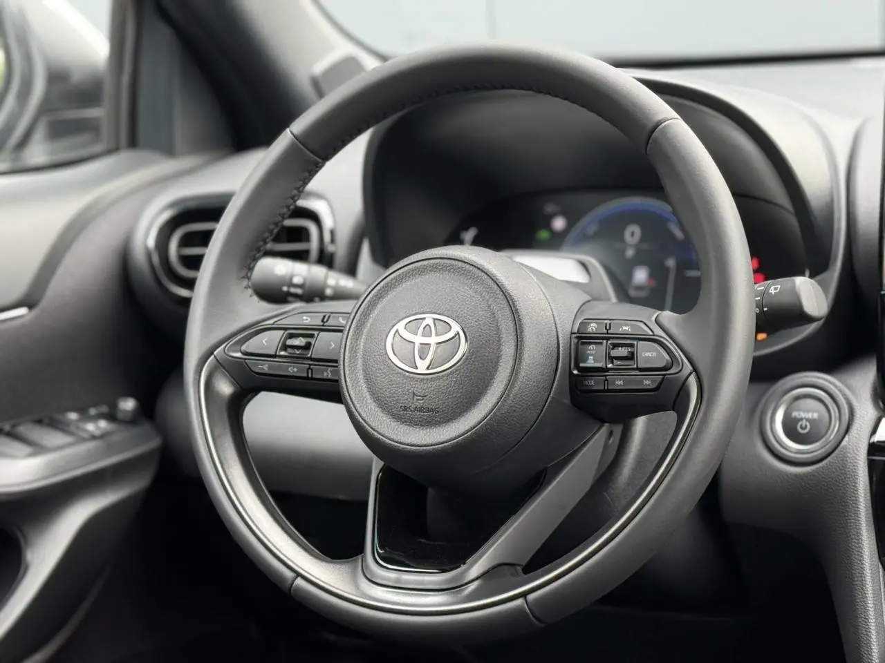 Vue rapprochée du volant cuir noir de la Toyota Yaris Cross 1.5 Hybrid 116 Design avec commandes intégrées.