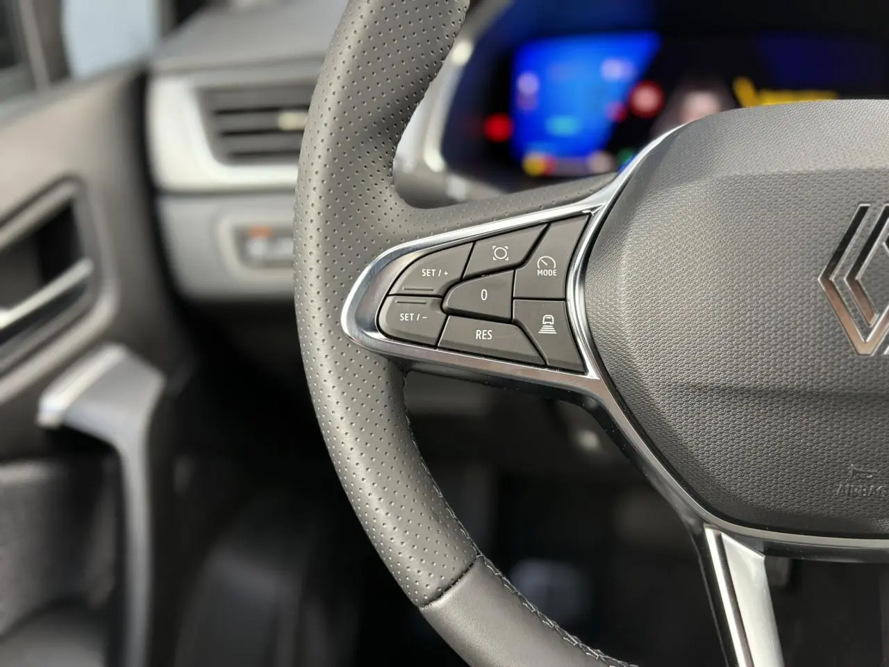 Gros plan sur le volant en cuir perforé avec commandes multifonctions du Renault SYMBIOZ noir étoile, tableau de bord flou en arrière-plan.