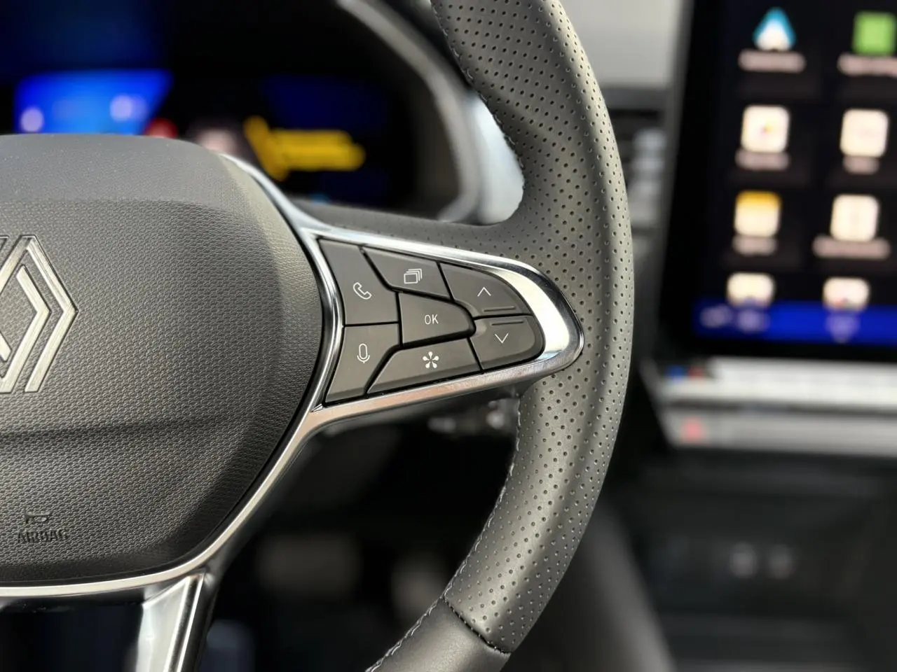 Gros plan sur le volant en cuir perforé de la Renault Symbioz 2025 avec commandes multifonctions et écran tactile flou en arrière-plan