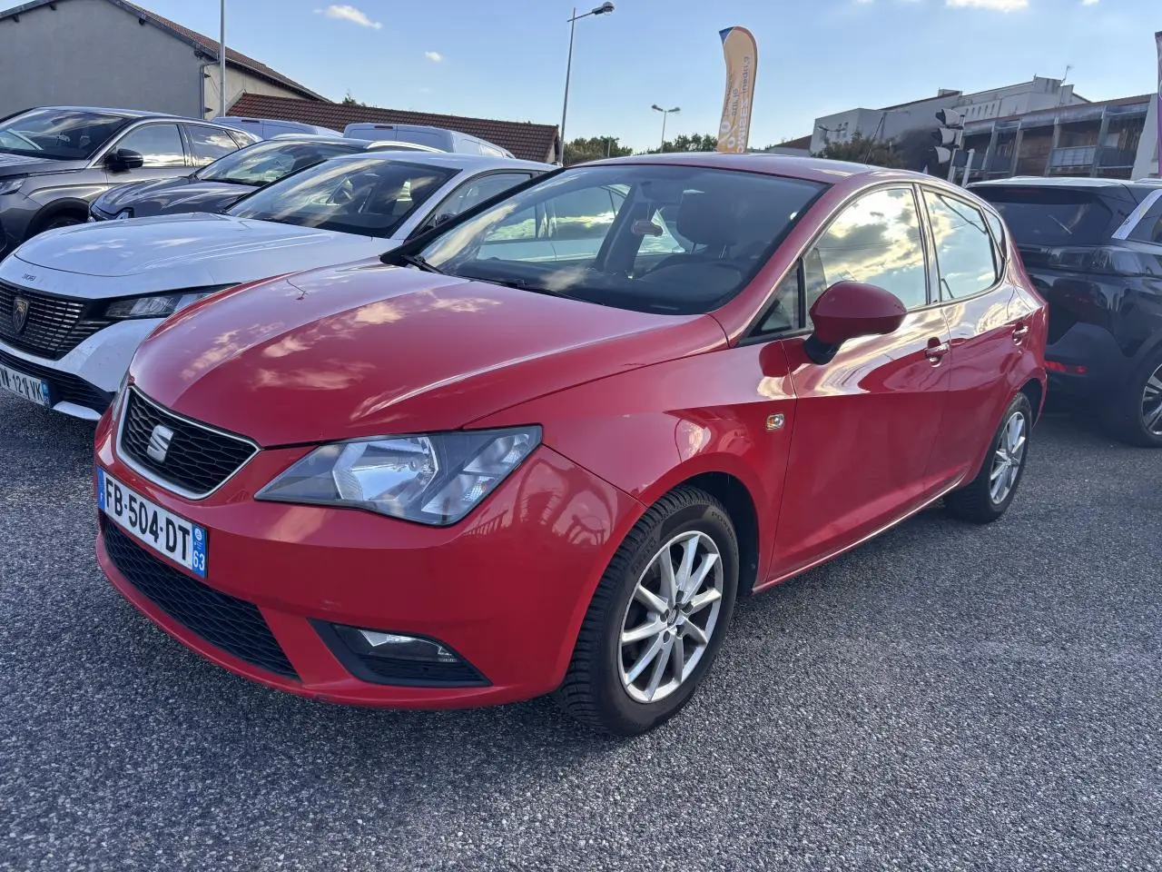 SEAT Ibiza 1.2 TSI rouge clair vue 3/4 avant droit sur parking avec jantes alliage et calandre noire.