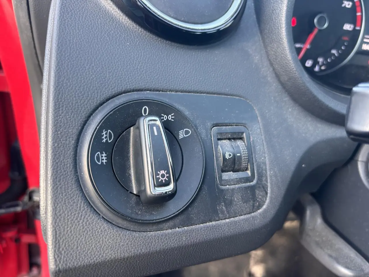 Gros plan sur le bouton de commande des phares à gauche du tableau de bord d'une SEAT Ibiza rouge clair de 2016.