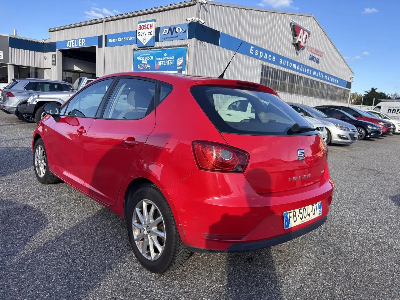 SEAT Ibiza rouge clair 2016 vue 3/4 arrière droit, compacte avec jantes alliage, stationnée devant un garage.
