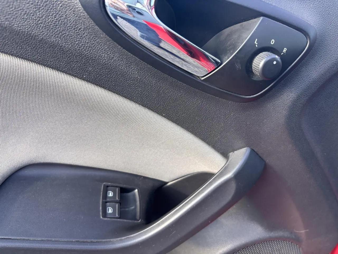 Détail de la porte côté conducteur d'une SEAT Ibiza 2016 rouge clair, avec commandes des vitres et réglage des rétroviseurs.