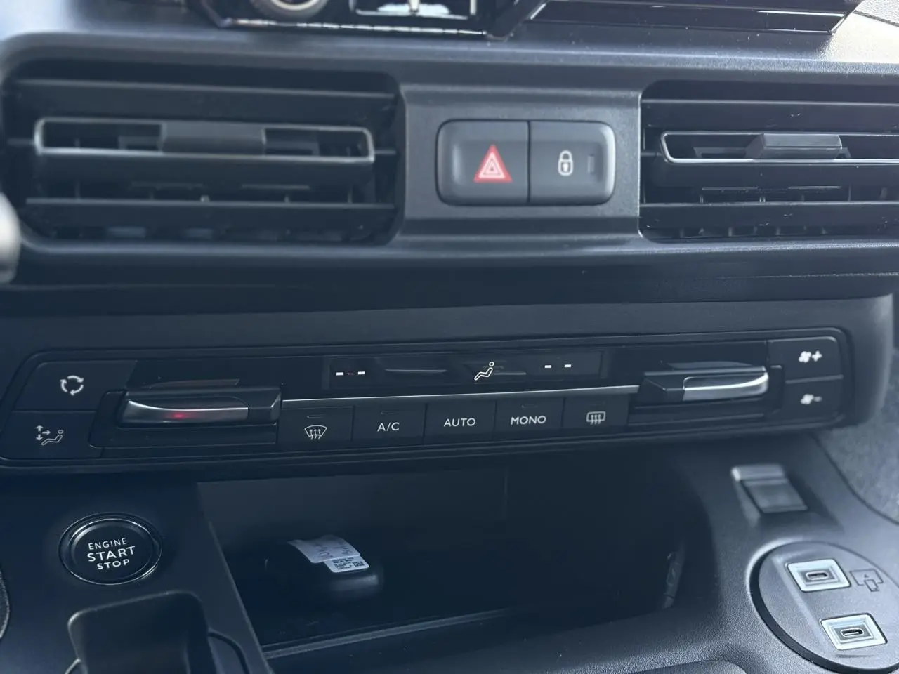 Gros plan sur la console centrale noire du Citroën Berlingo Multispace 2025, montrant les commandes de climatisation et le bouton start-stop.