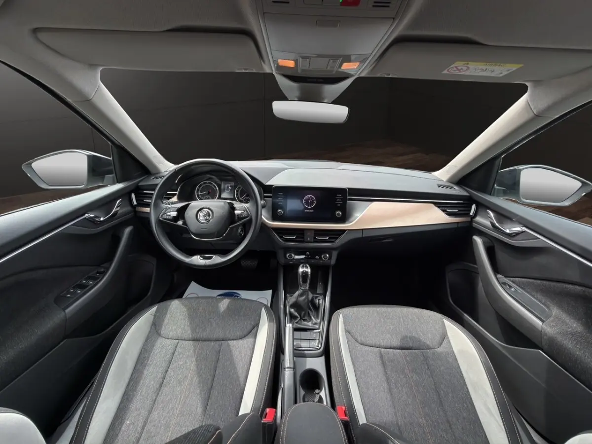 Vue intérieure côté conducteur du Skoda Kamiq gris clair 2023, montrant sièges tissu bicolore et tableau de bord bois clair.