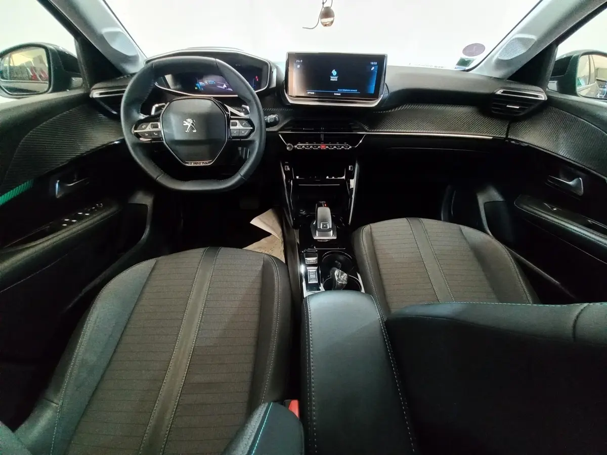 Vue intérieure avant de la Peugeot 208 noire, montrant le volant compact, l'écran tactile central et les sièges tissu gris.