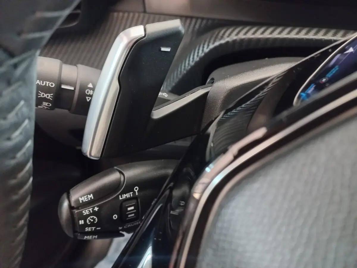 Gros plan sur la commande de régulateur de vitesse et palettes au volant du tableau de bord noir d’une Peugeot 208 2022.