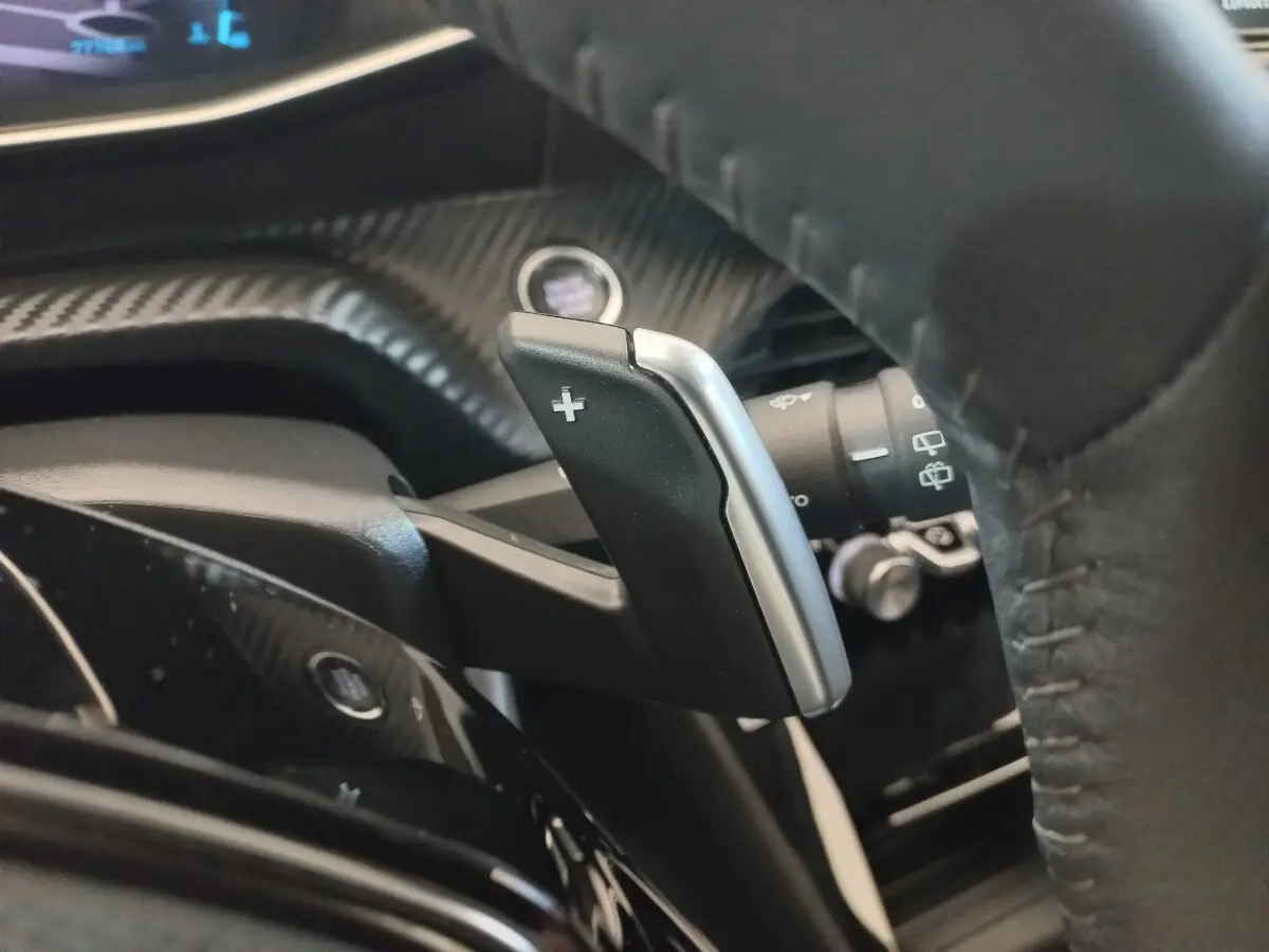 Gros plan sur la palette de changement de vitesse droite en plastique noir et argent, volant cuir noir de la Peugeot 208 2022.