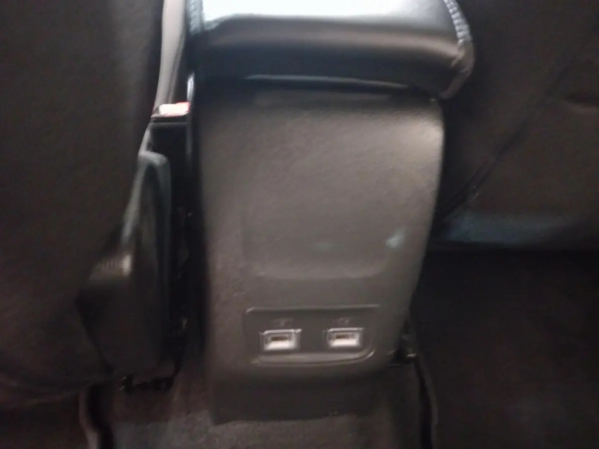 Gros plan sur la console arrière noire de la Peugeot 208 avec deux ports USB visibles au bas des sièges avant.