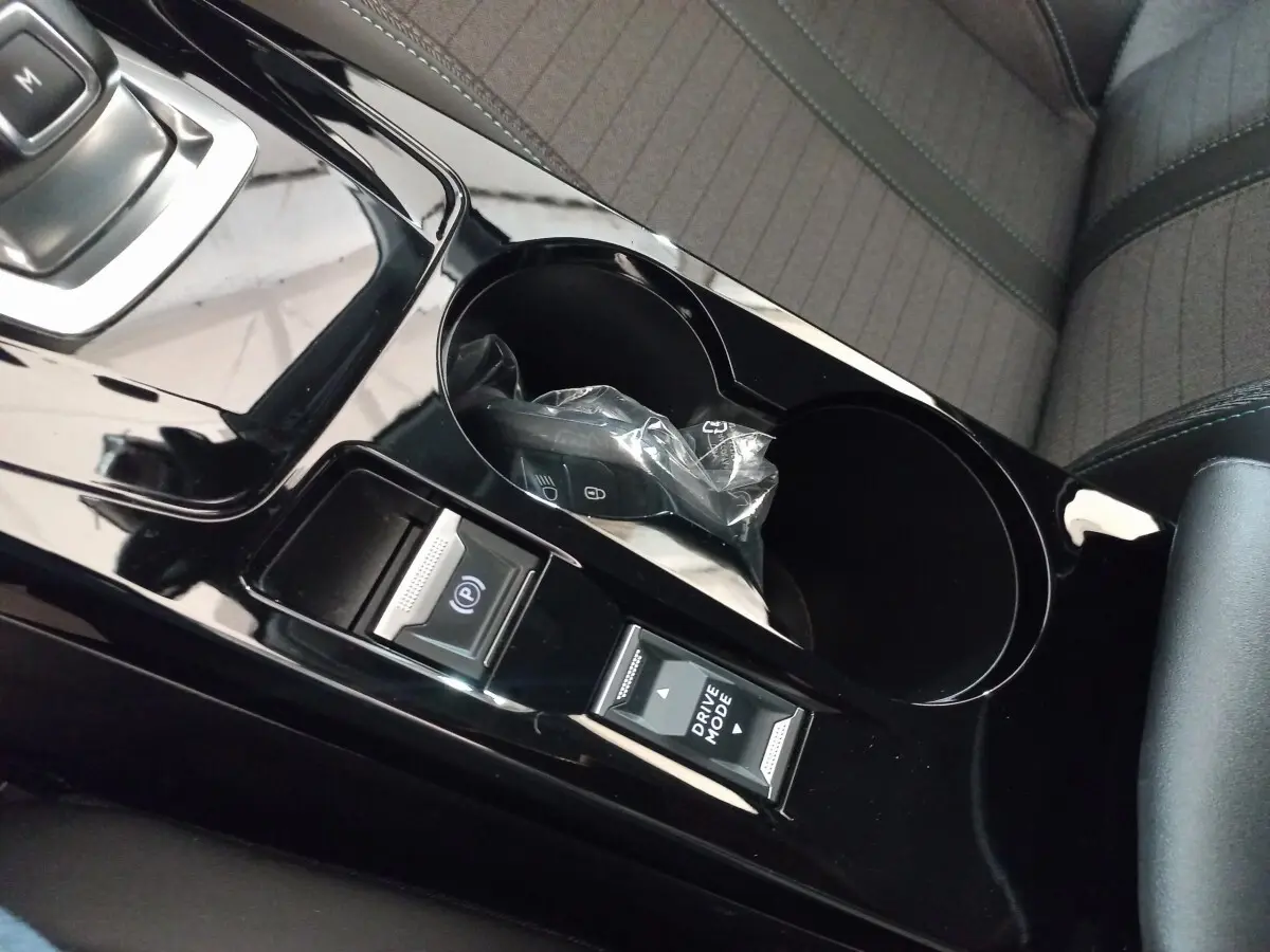 Gros plan sur la console centrale noire brillante de la Peugeot 208 PureTech 100, avec boutons frein à main et mode de conduite.