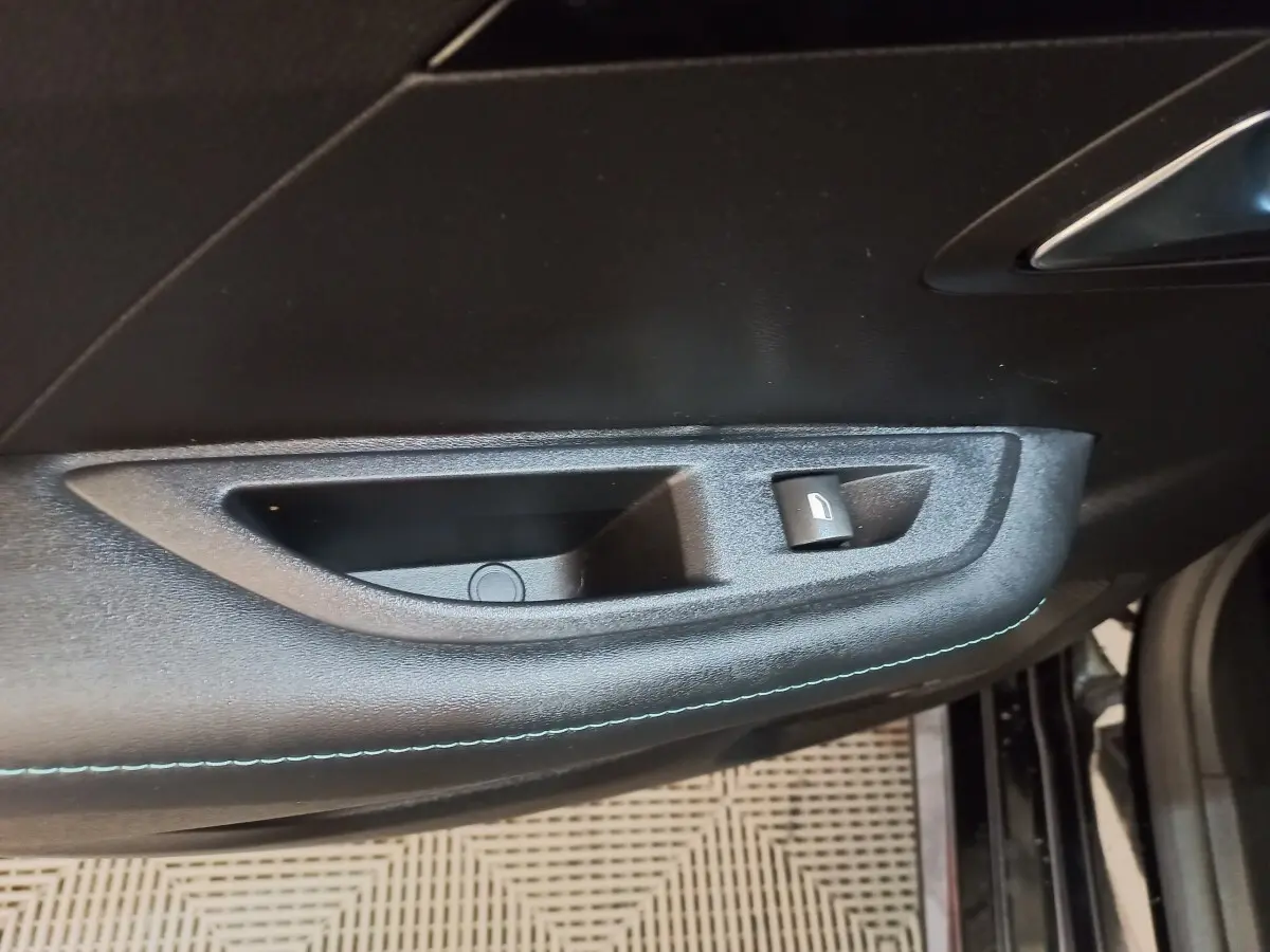 Détail de la poignée intérieure de porte côté gauche d’une Peugeot 208 noire, avec bouton de verrouillage.