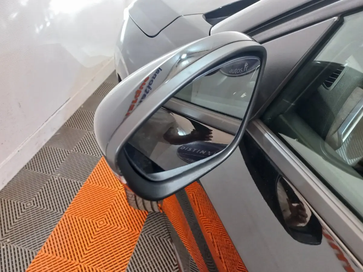 Rétroviseur côté gauche d’une Peugeot 208 noire, vue rapprochée avec reflet du sol orange et gris.