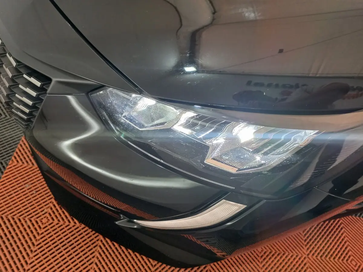Gros plan sur le phare avant gauche noir brillant de la Peugeot 208 PureTech 100 S&S EAT8 Allure Pack 2022.