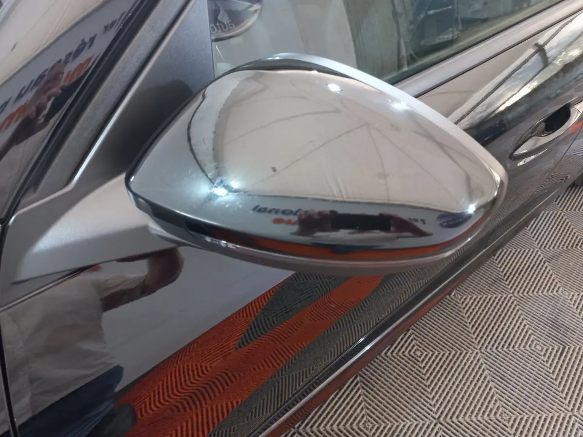 Rétroviseur chromé côté droit d'une Peugeot 208 noire, vue rapprochée avec reflet de l'environnement intérieur.