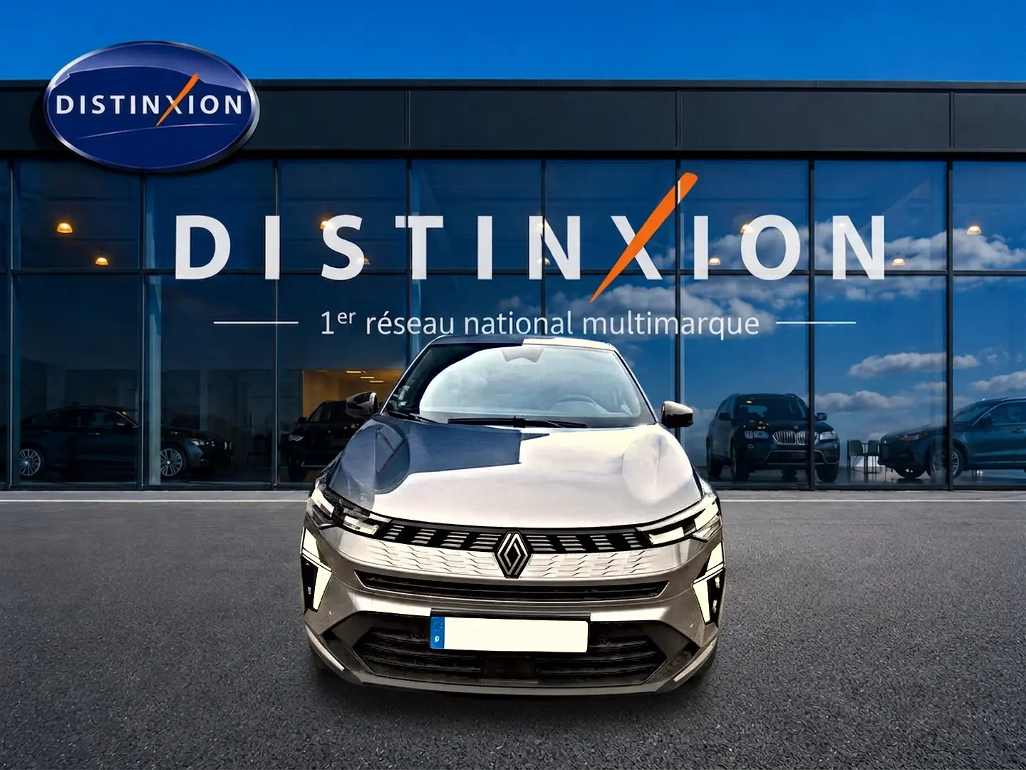 Vue frontale d'une Renault SYMBIOZ gris cassiopé avec calandre distinctive et feux LED, devant un showroom Distinxion.