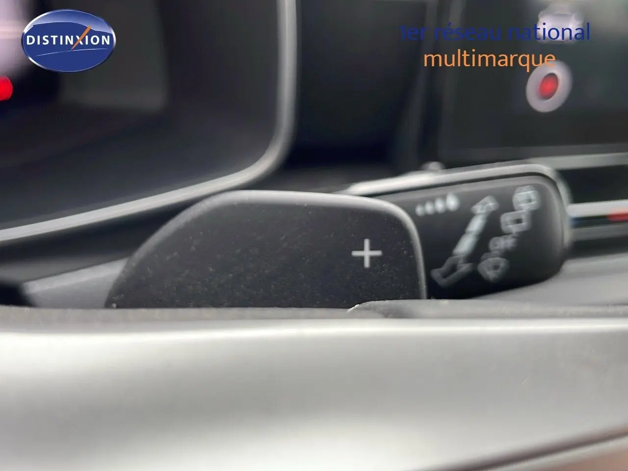 Gros plan sur la palette de changement de vitesse "+" du volant d'une SEAT LEON ST 2023 gris urbain, intérieur moderne.