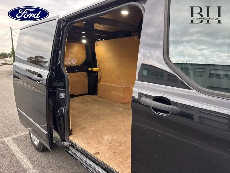 Vue latérale droite du Ford Transit Custom noir Agate métallisé avec porte coulissante ouverte révélant l'intérieur en bois du fourgon.