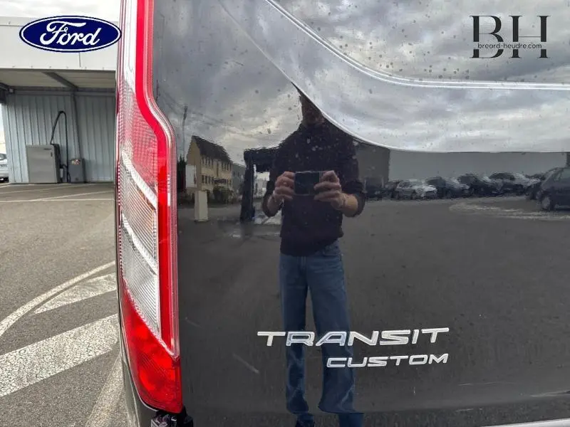 Gros plan sur le feu arrière gauche et le logo Transit Custom du fourgon Ford noir Agate métallisé 2023.