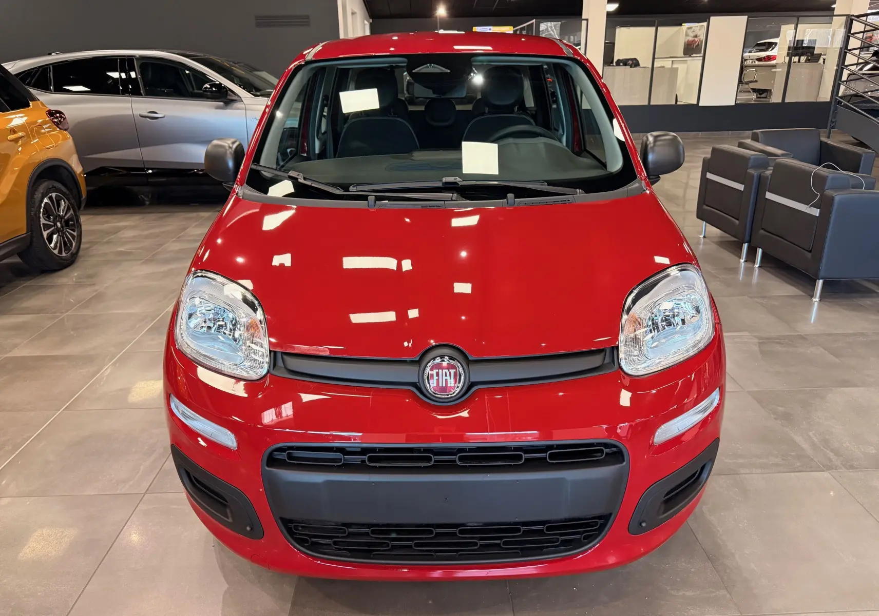 Vue frontale d'une FIAT Panda 1.0 70 CH Hybrid City rouge Amore en showroom, avec calandre noire et phares arrondis.