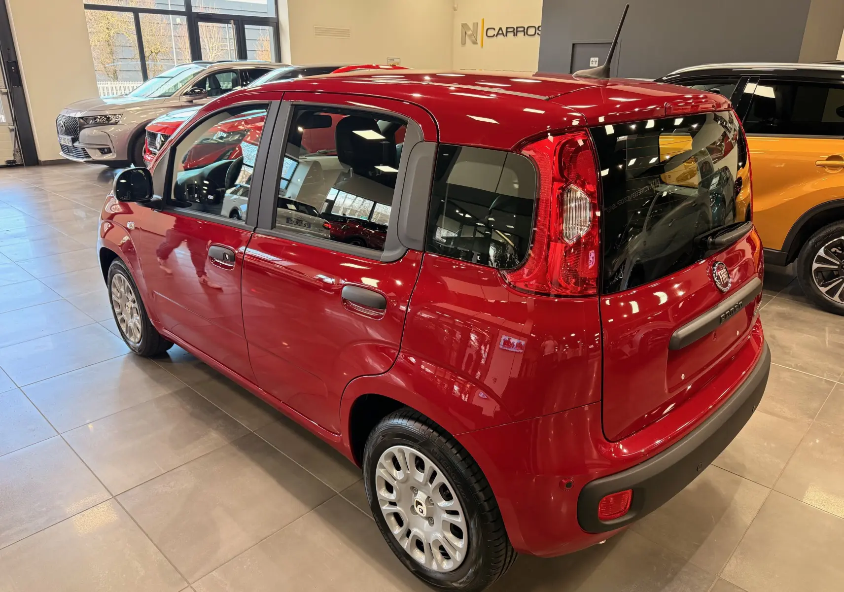 Vue 3/4 arrière droite d'une Fiat Panda 1.0 70 CH Hybrid City rouge Amore en showroom avec détails noirs contrastants.