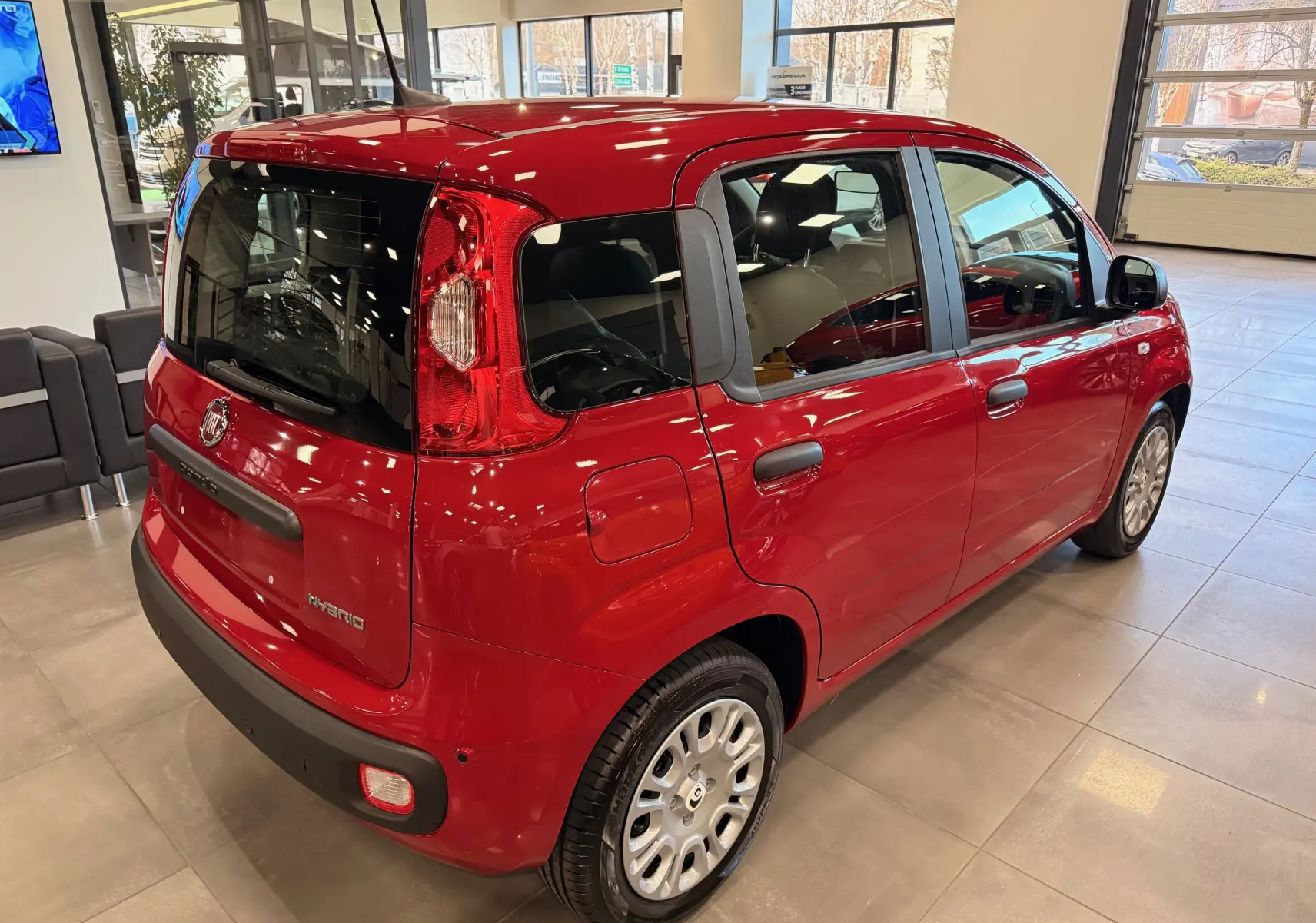 Vue 3/4 arrière droite d'une Fiat Panda 1.0 Hybrid rouge Amore en showroom, avec détails noirs contrastants et jantes argentées.