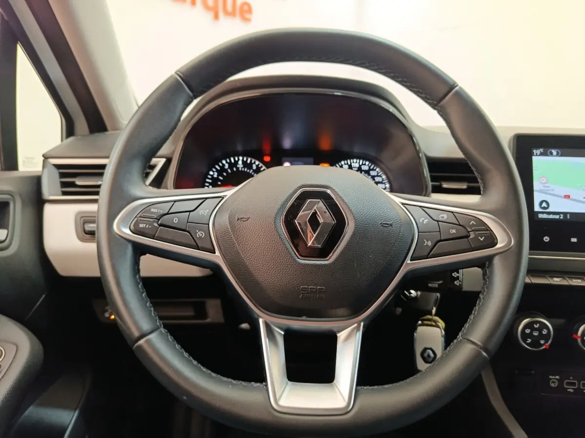 Vue rapprochée du volant cuir noir de la Renault Clio 2023 avec commandes multifonctions et tableau de bord éclairé.