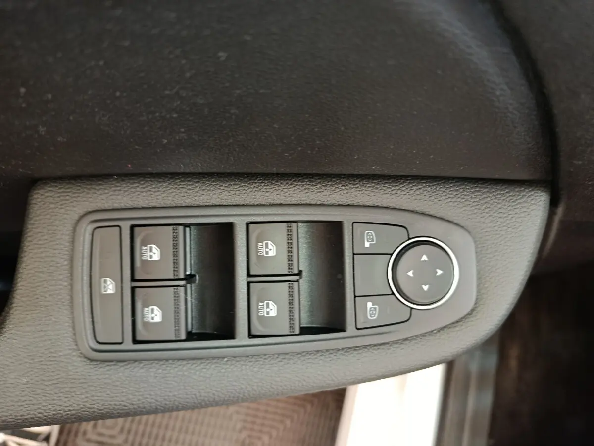 Gros plan sur les commandes de lève-vitres et rétroviseurs côté conducteur d’une Renault Clio blanche 2023.