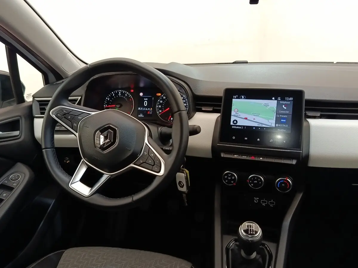 Vue intérieure avant de la Renault Clio blanche 2023, volant cuir multifonctions et écran tactile de navigation visible.