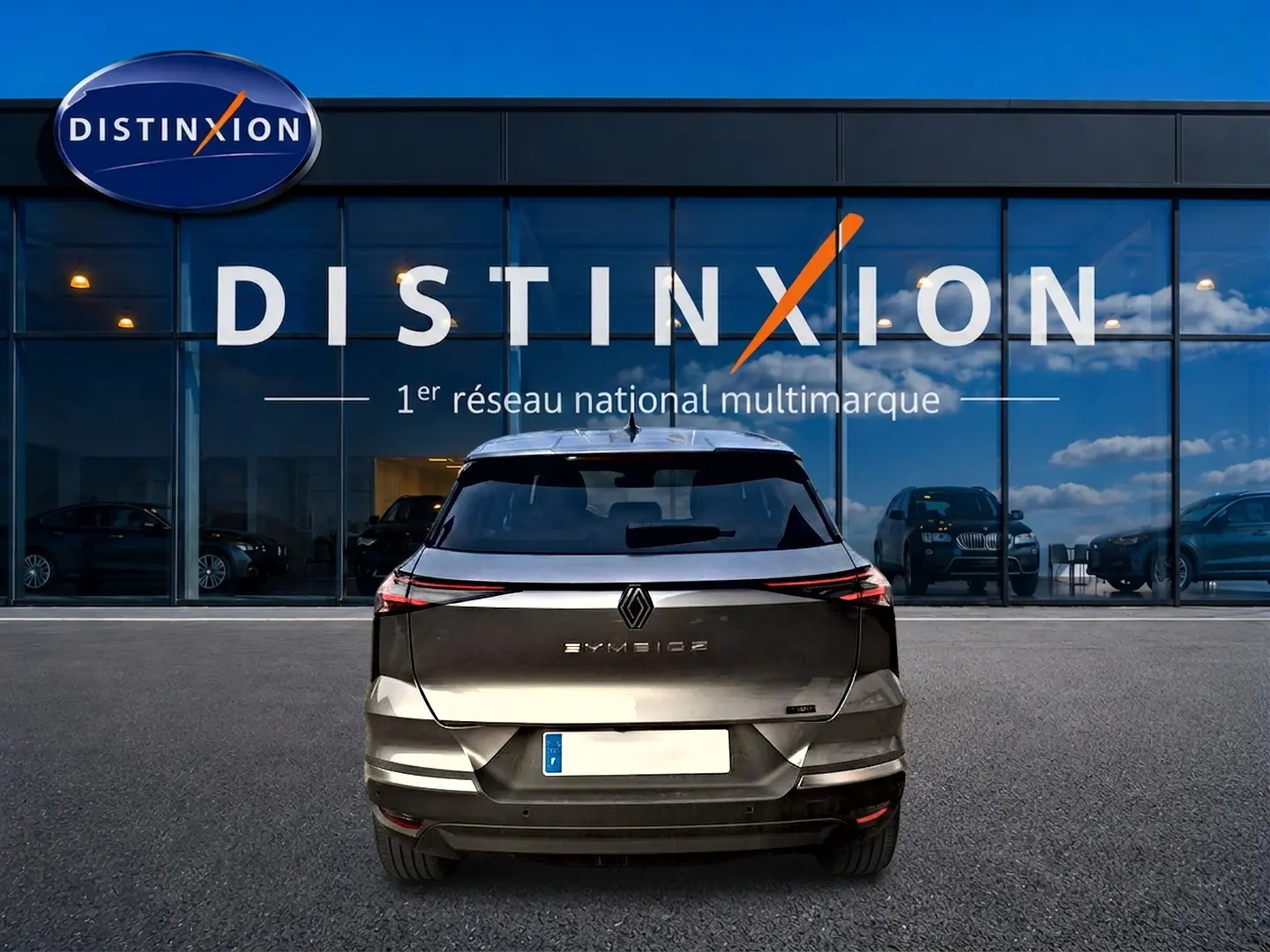 Vue arrière d'une Renault SYMBIOZ gris cassiopée garée devant une vitrine avec logo Distinxion.