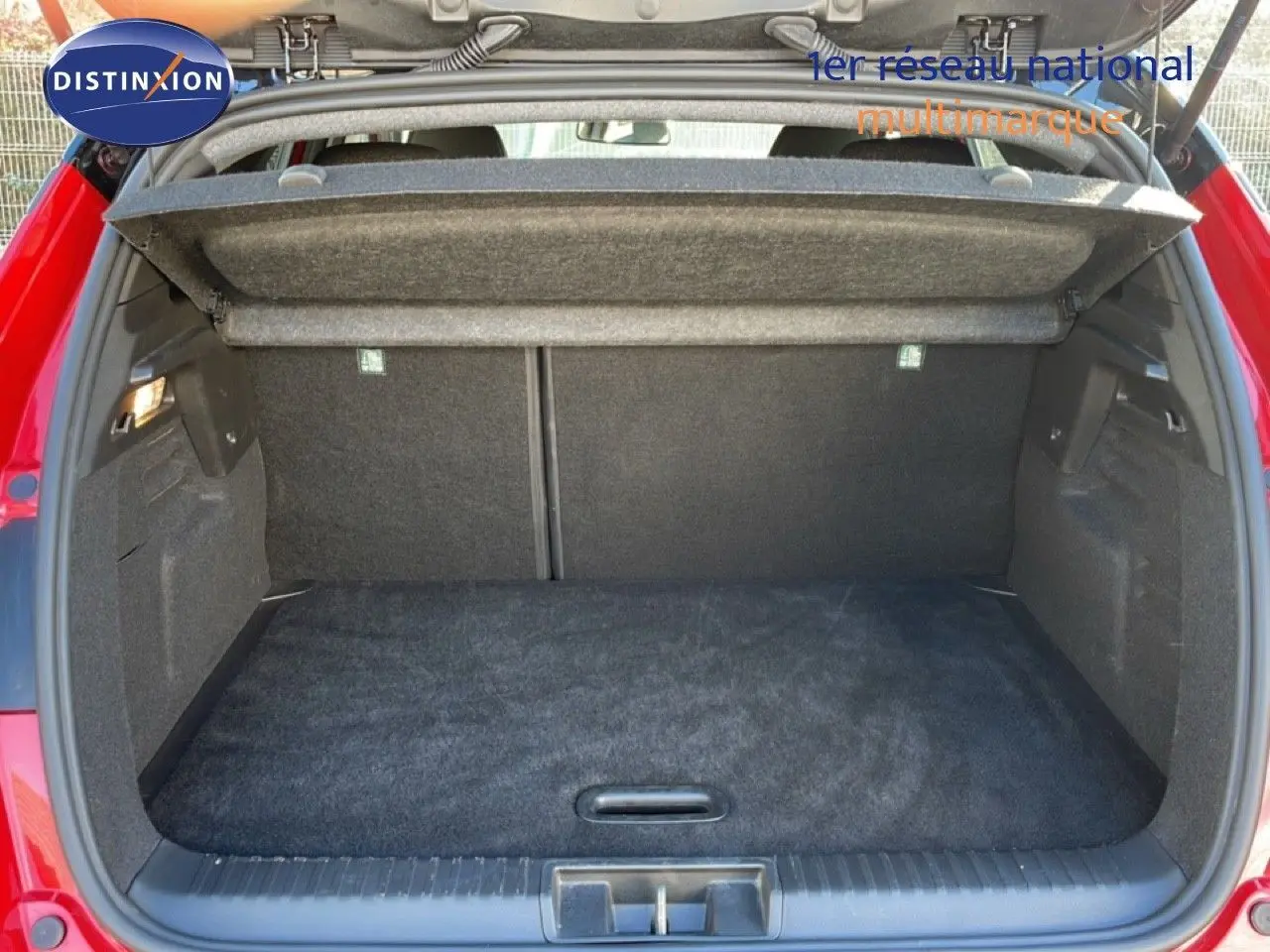 Coffre ouvert vu de l'arrière d'un Renault Captur 2025 rouge désir métal avec toit noir, intérieur de coffre en tissu gris.
