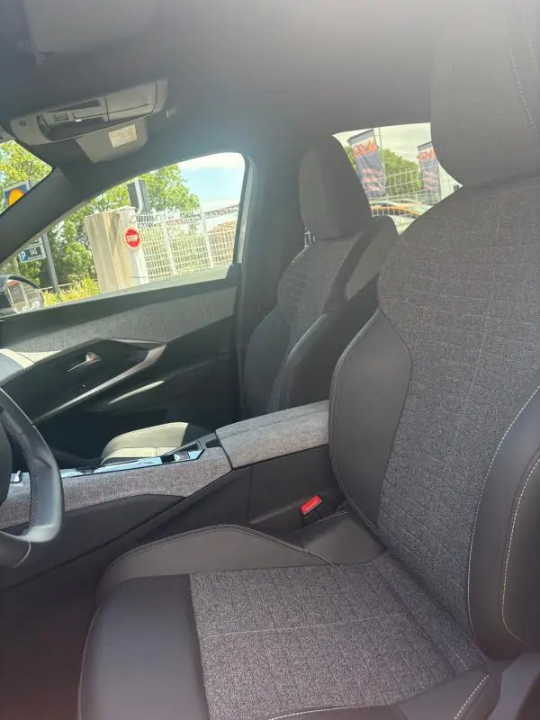 Intérieur du Peugeot 3008 Hybrid 136 e-DCS6 Allure 2025, vue côté conducteur sur sièges tissu gris clair et cuir noir.