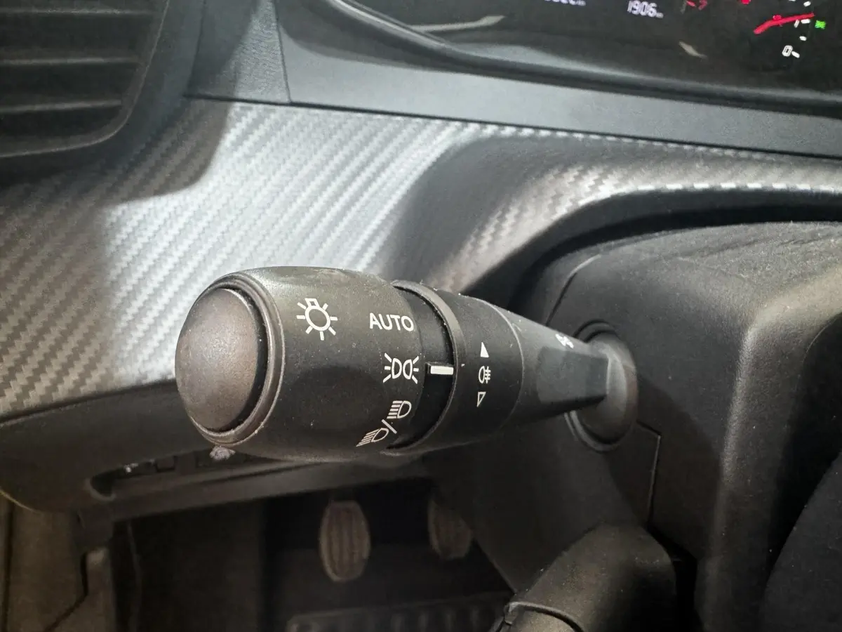 Gros plan sur la manette de commande des phares à gauche du volant dans l’habitacle de la Peugeot 208 jaune.