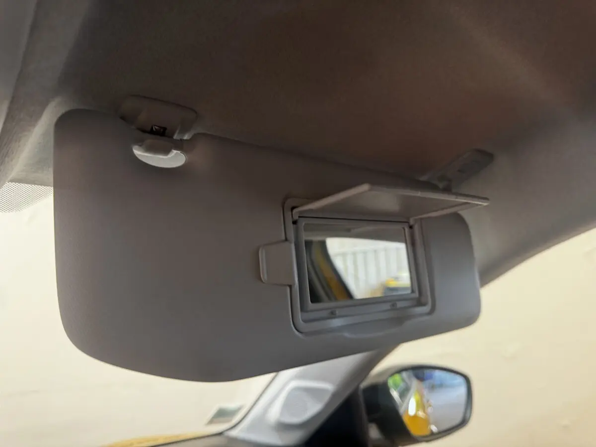 Détail du pare-soleil côté conducteur avec miroir de courtoisie ouvert dans une Peugeot 208 jaune visible en reflet.