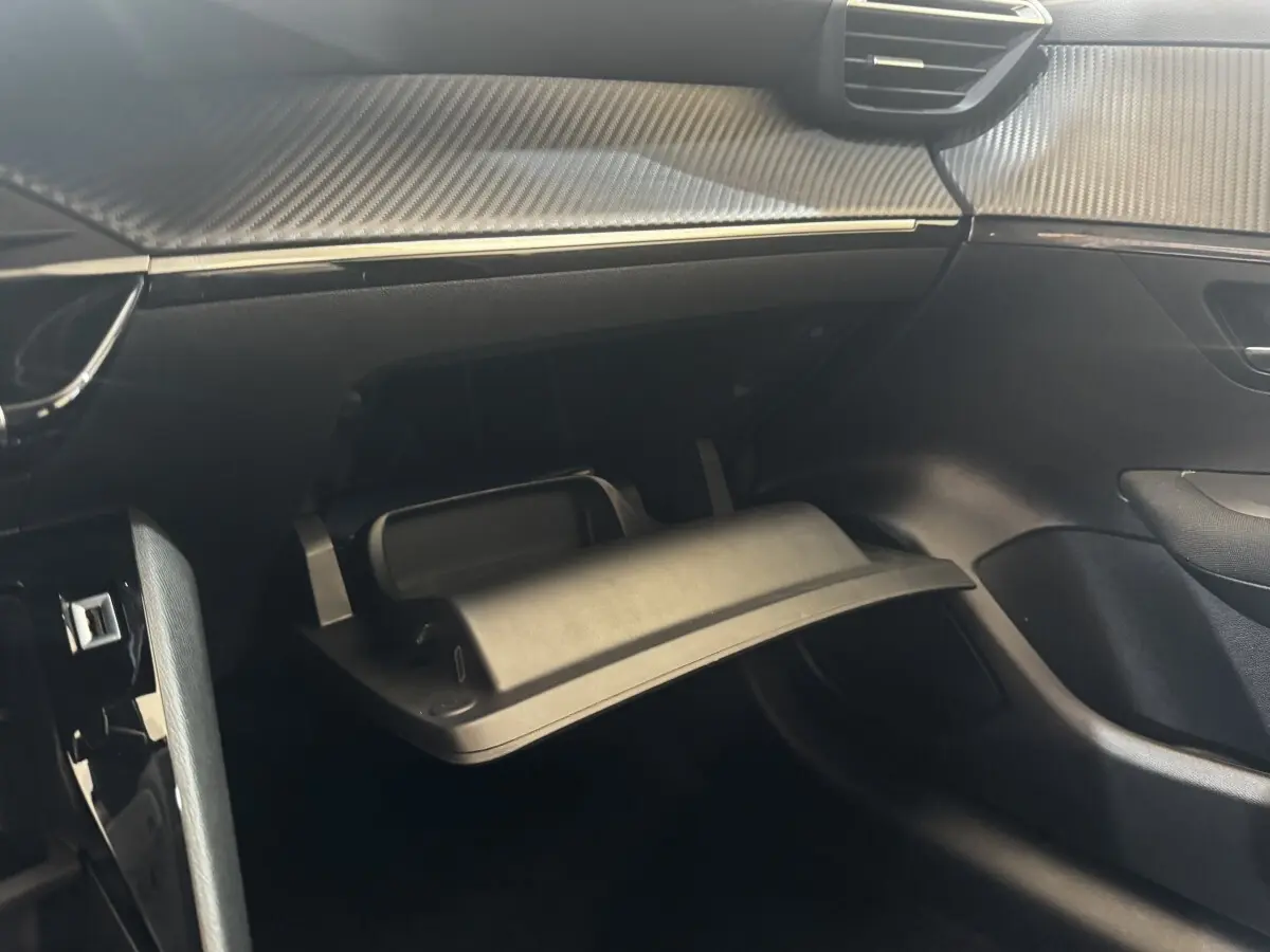 Vue intérieure côté passager de la Peugeot 208 jaune 2023, avec boîte à gants ouverte et tableau de bord noir.