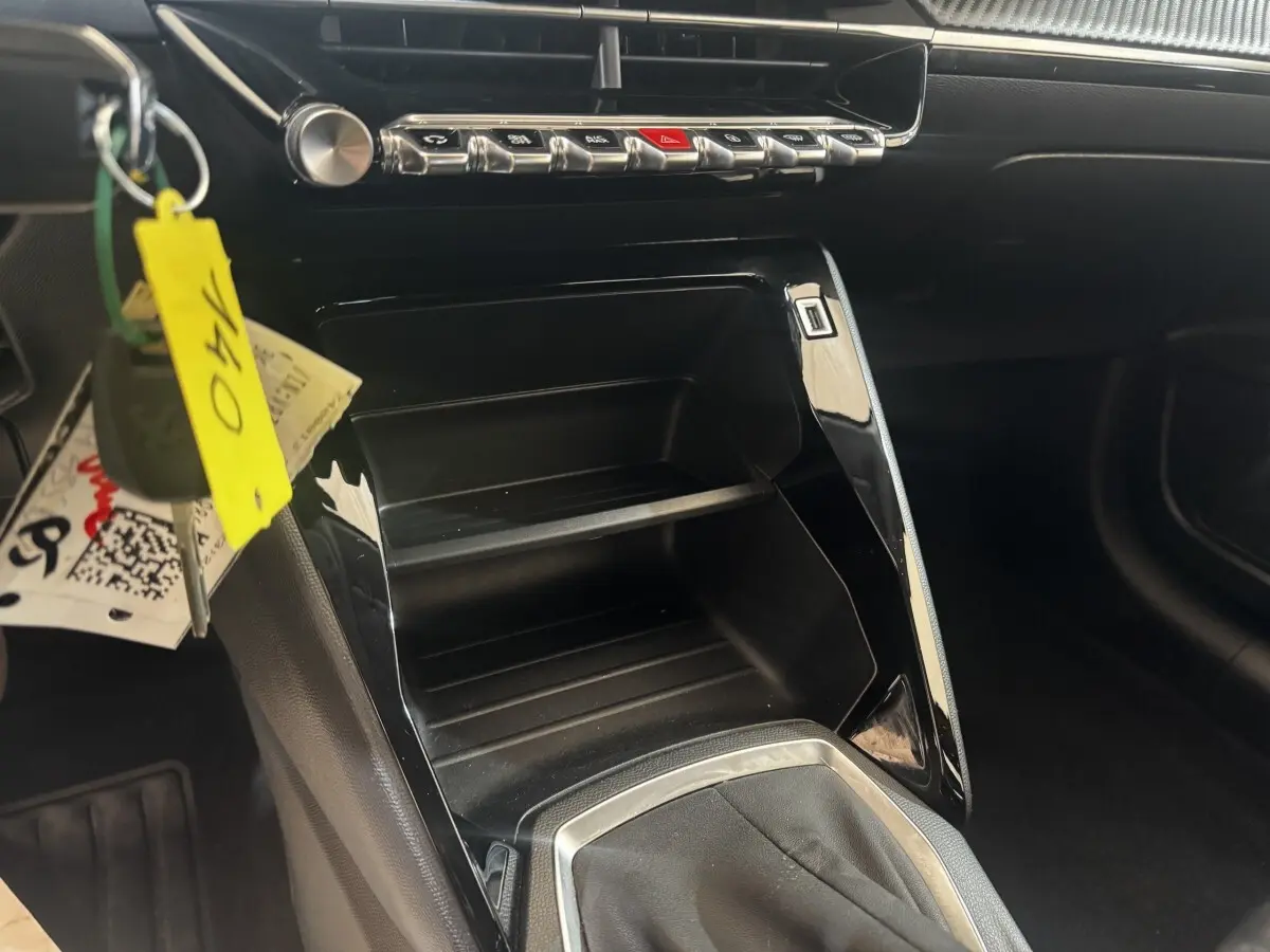 Vue intérieure centrée sur la console centrale noire brillante de la Peugeot 208 jaune, avec clés suspendues visibles.
