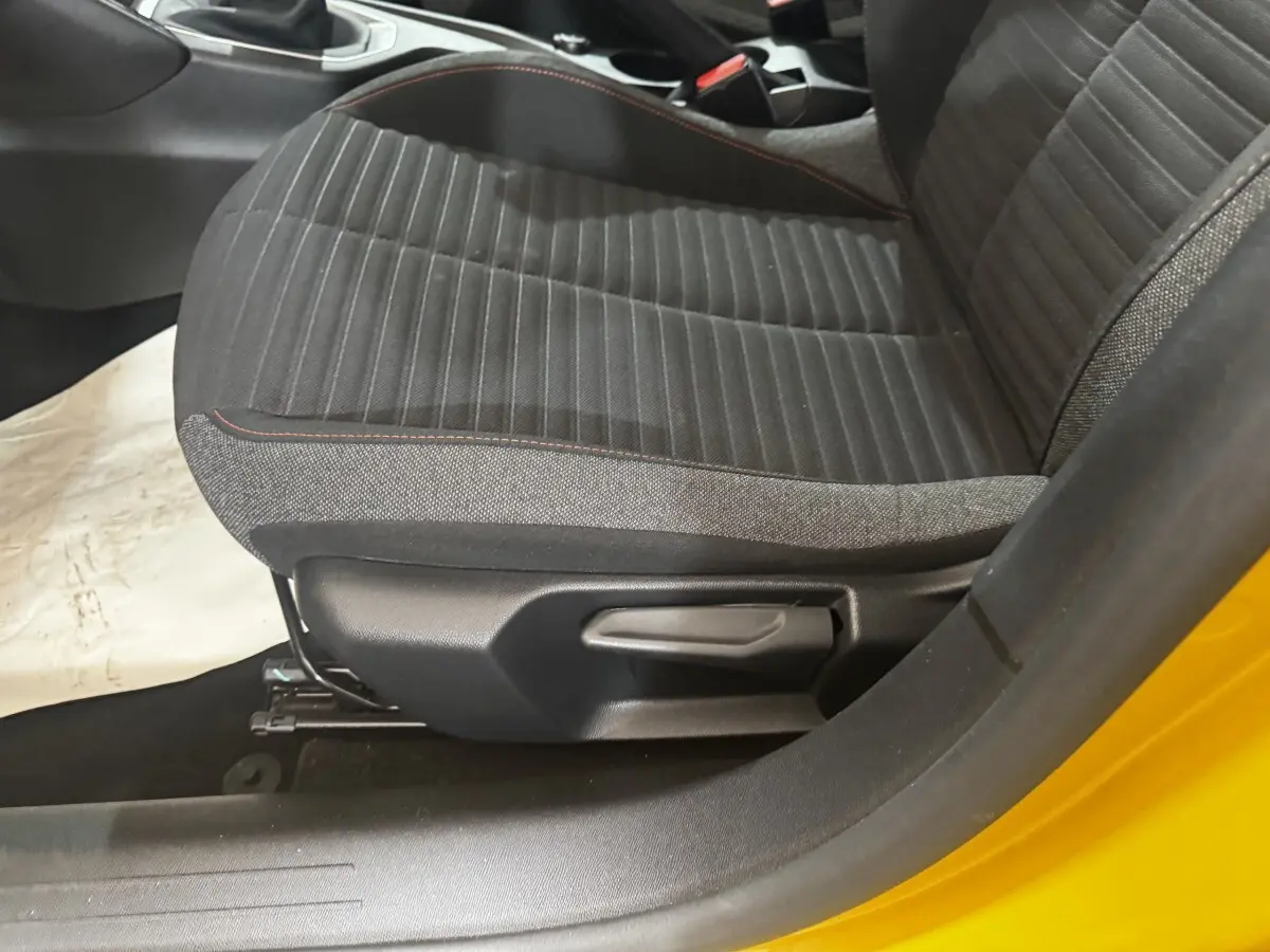 Gros plan sur le siège avant gauche noir avec surpiqûres rouges, porte ouverte d'une Peugeot 208 jaune.