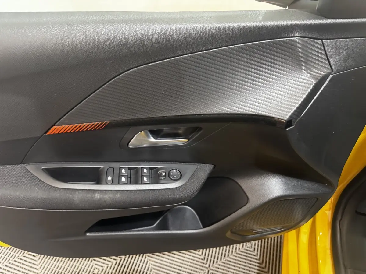 Vue intérieure côté conducteur de la porte noire avec insert effet carbone et détail orange sur Peugeot 208 jaune 2023.