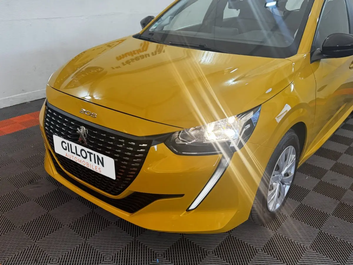 Vue 3/4 avant droite d'une Peugeot 208 jaune avec phares allumés et calandre noire distinctive.