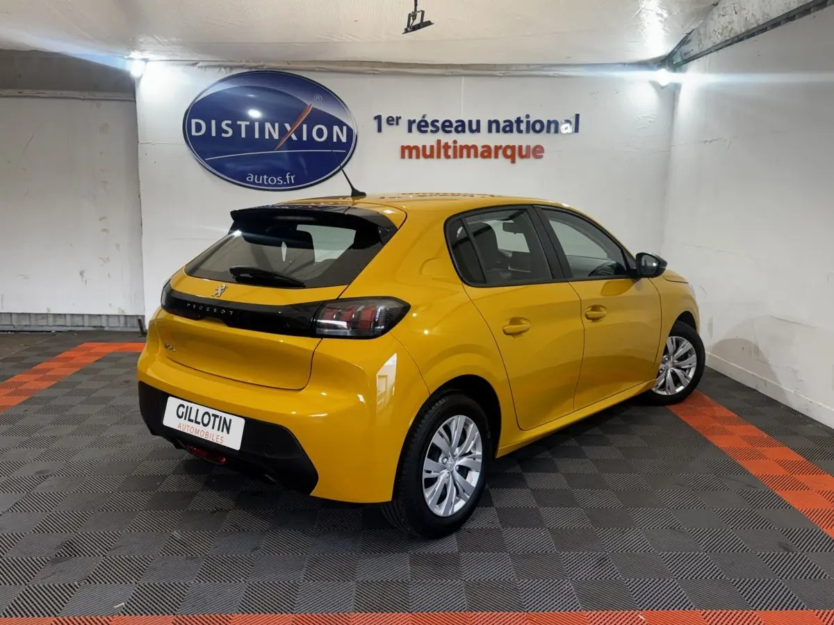 Vue 3/4 arrière droite d'une Peugeot 208 jaune vif stationnée en intérieur avec feux arrière sombres et jantes argentées.